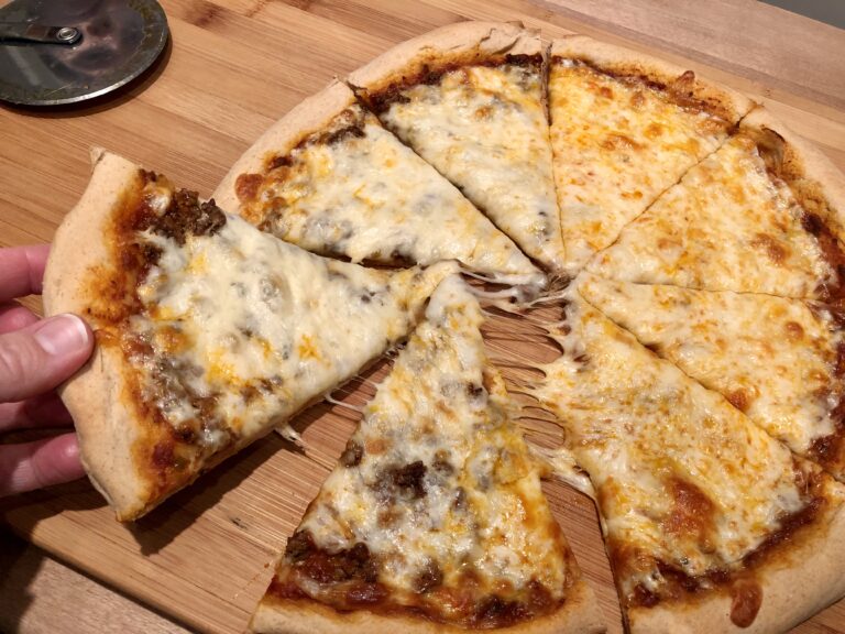 round pizza, cut into 8 slices with one slice being pulled away. Pizza is covered in melted cheese and toppings.