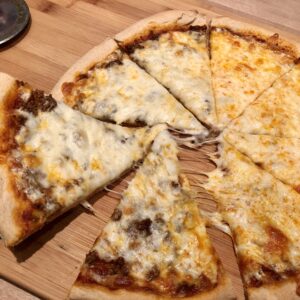 round pizza, cut into 8 slices with one slice being pulled away. Pizza is covered in melted cheese and toppings.