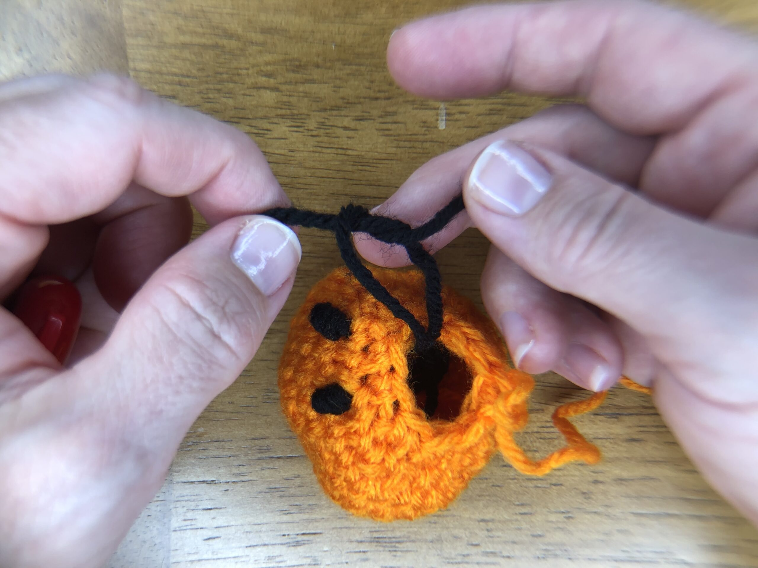 attaching black yarn eyes to orange baby pumpkin