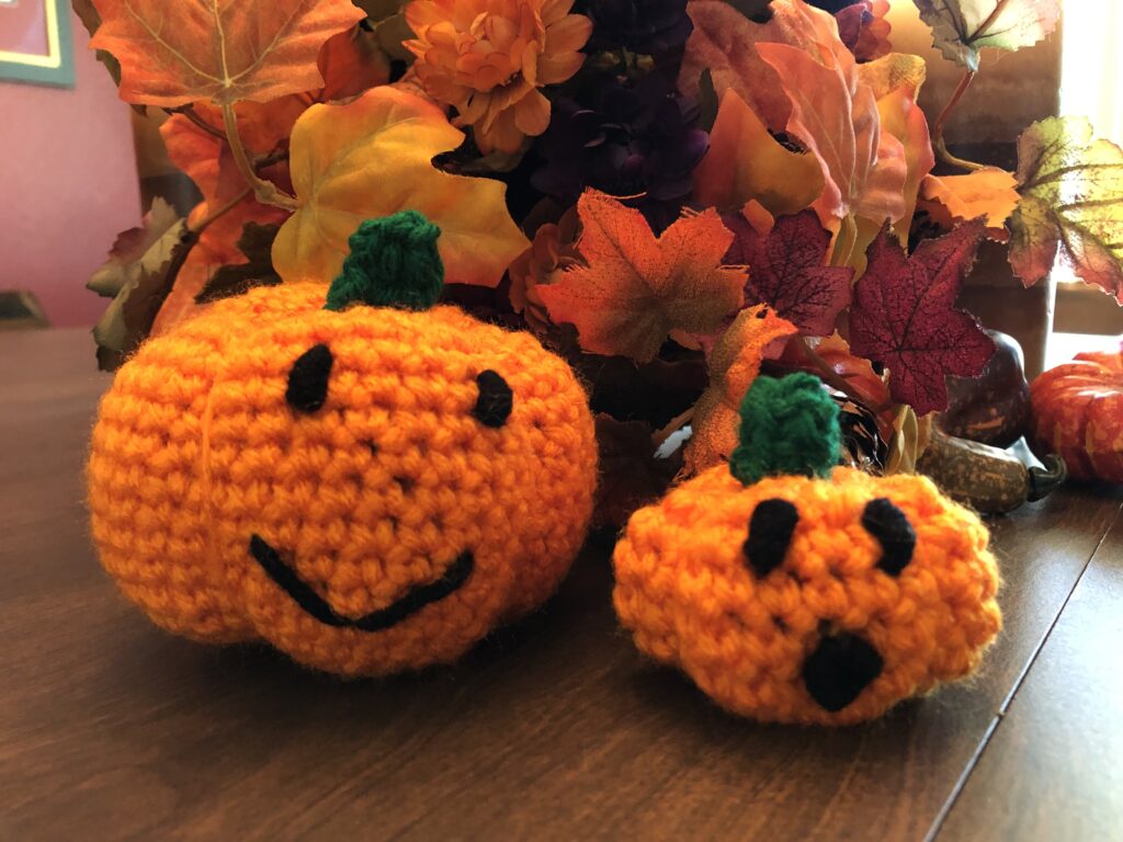 small crocheted jack-o-lantern pumpkins in front of fall colored leaves