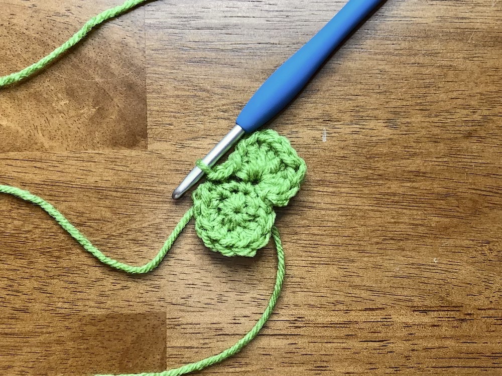 small green crocheted circle starting the 3rd round with the first leaf created