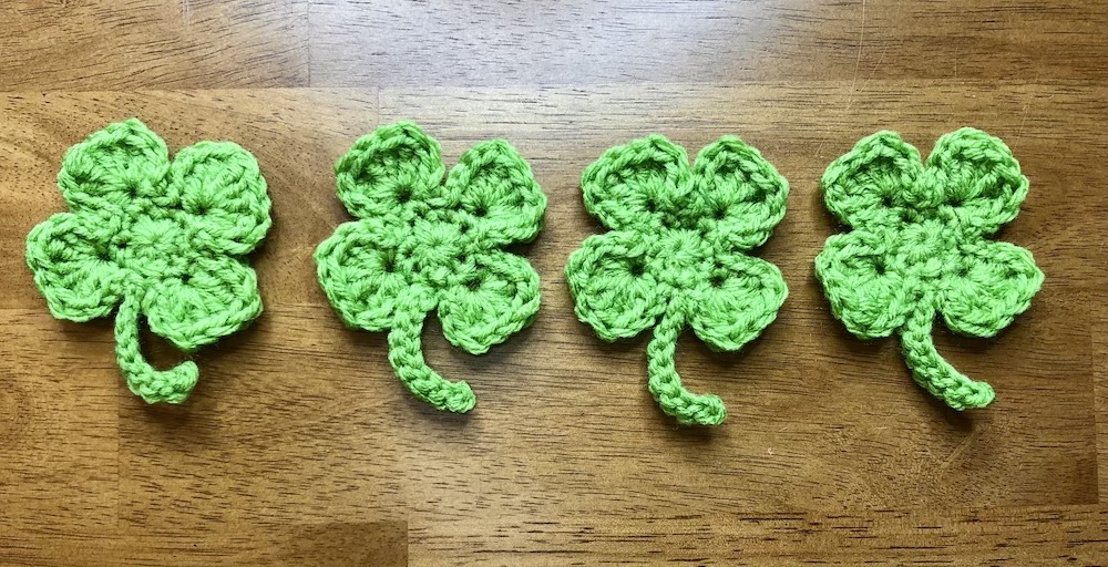 4 small crocheted shamrocks in a row
