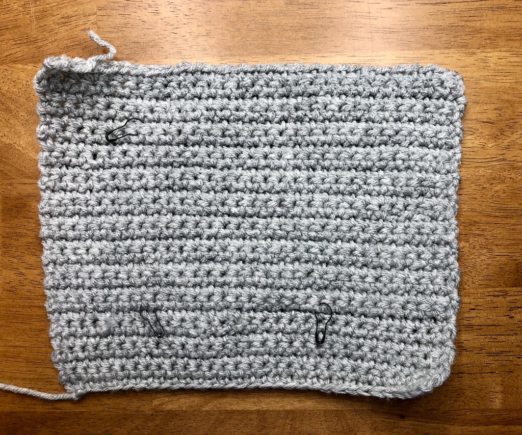 How to make a crochet swatch using light grey yarn and the single crochet stitch, with markers placed to help with measuring. 