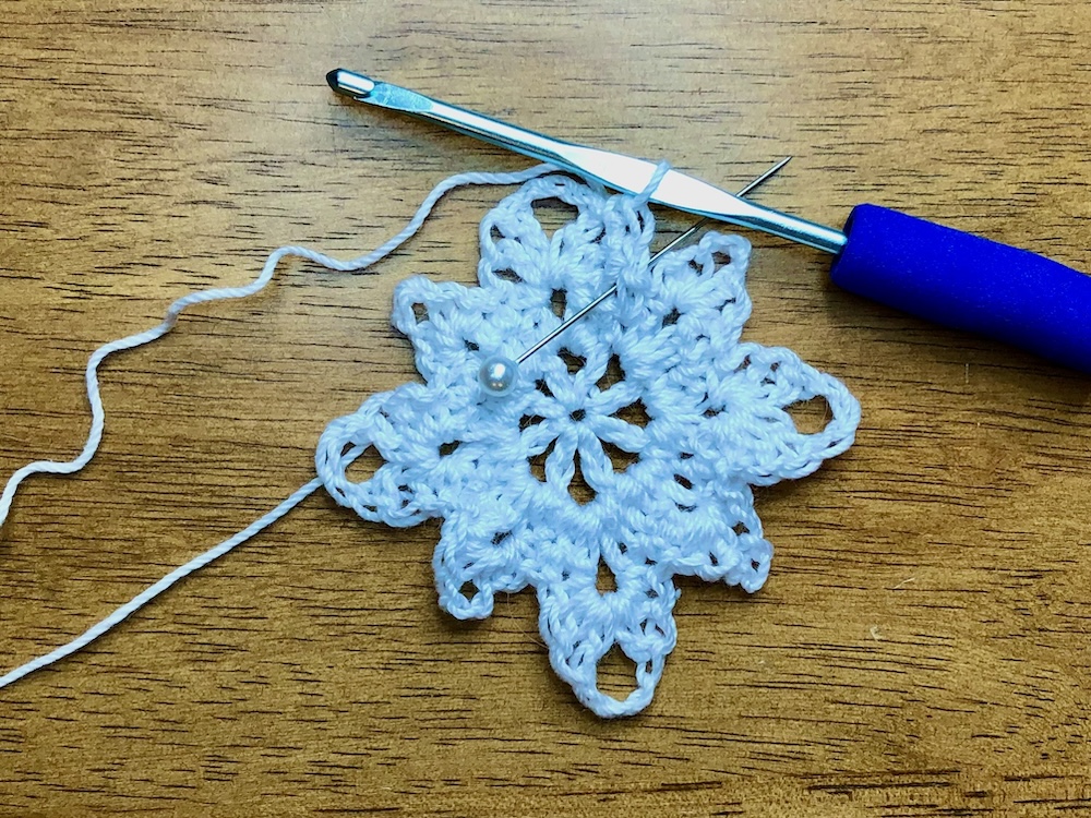 white christmas star ornament with pin showing location for last stitch in round 3