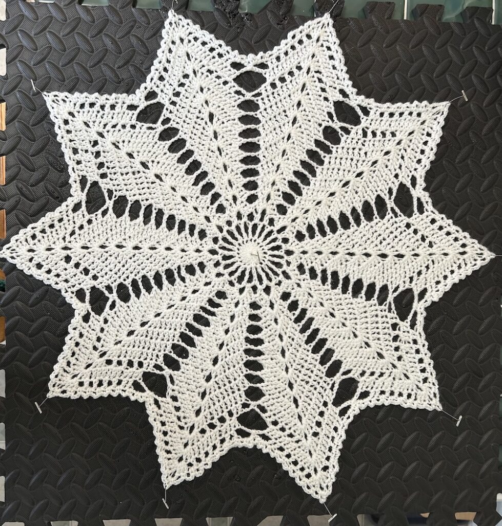 white star doily pinned to a dark gray blocking mat