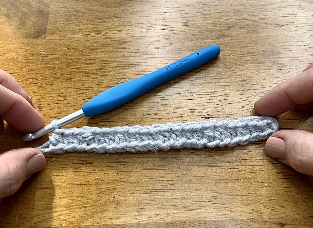 light gray crocheted row of half double crochet stitches on a wooden background