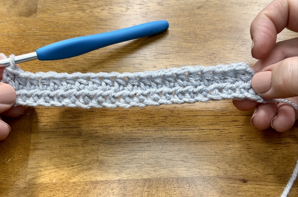 light gray crocheted piece showing two rows of half double crochet stitches on a wooden background