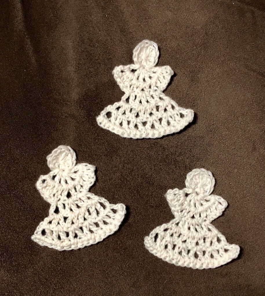 three small white crocheted angels on a dark brown background