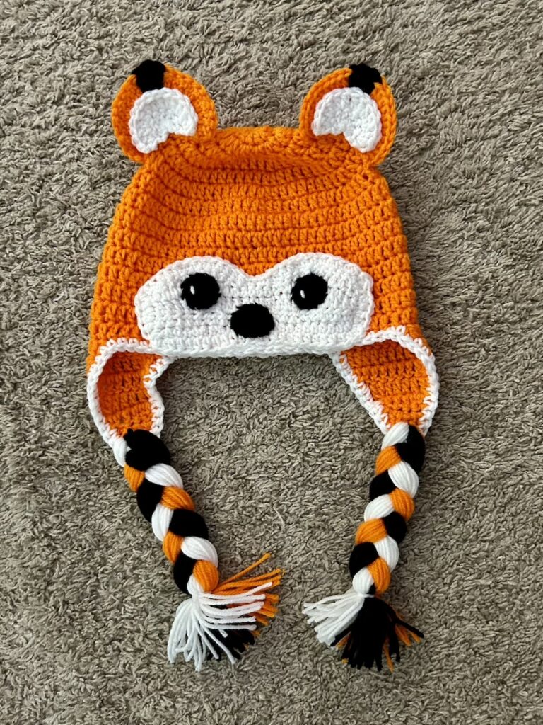 orange white and black crocheted fox hat on a tan background.