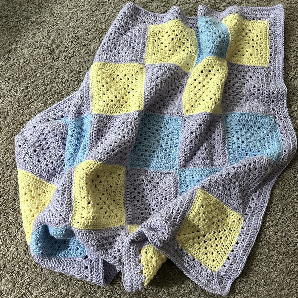 crocheted granny square blanket in lavender, yellow and blue.