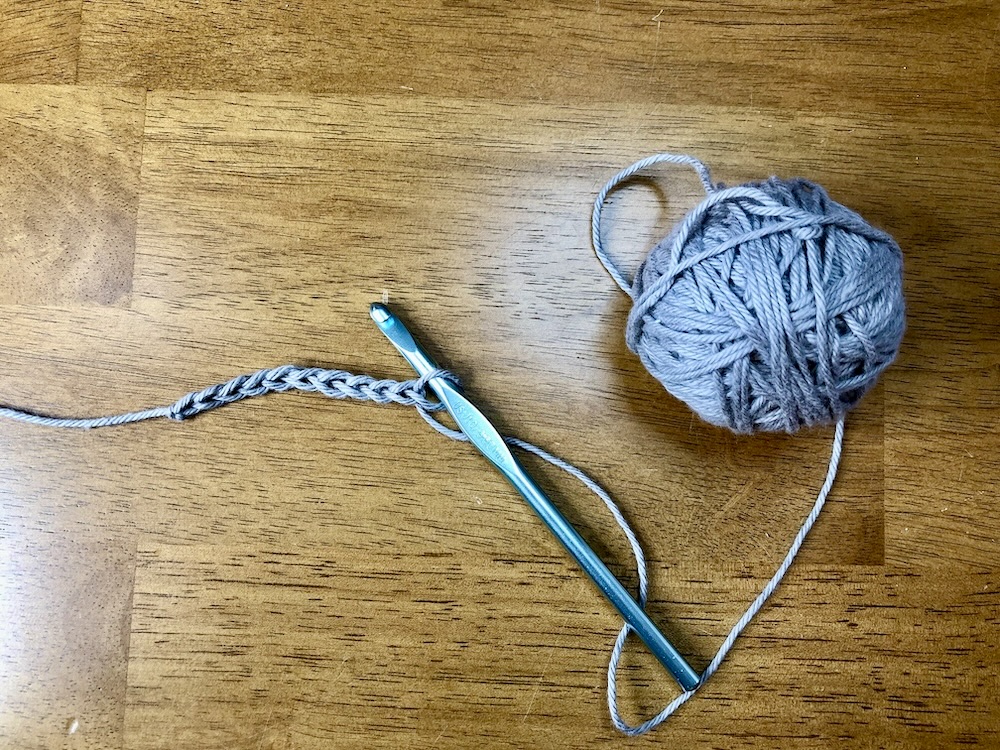 ball of gray yarn with a crochet hook and a foundation chain on a wooden background.