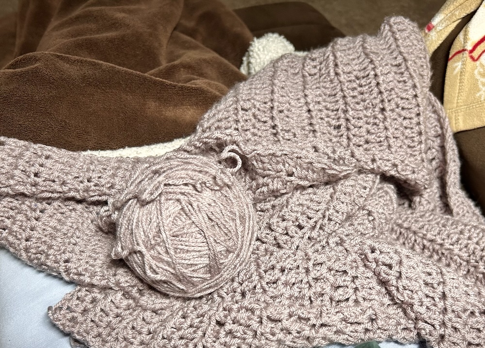 lavender gray crocheted sweater and a ball of yarn being taken apart to reuse the yarn.