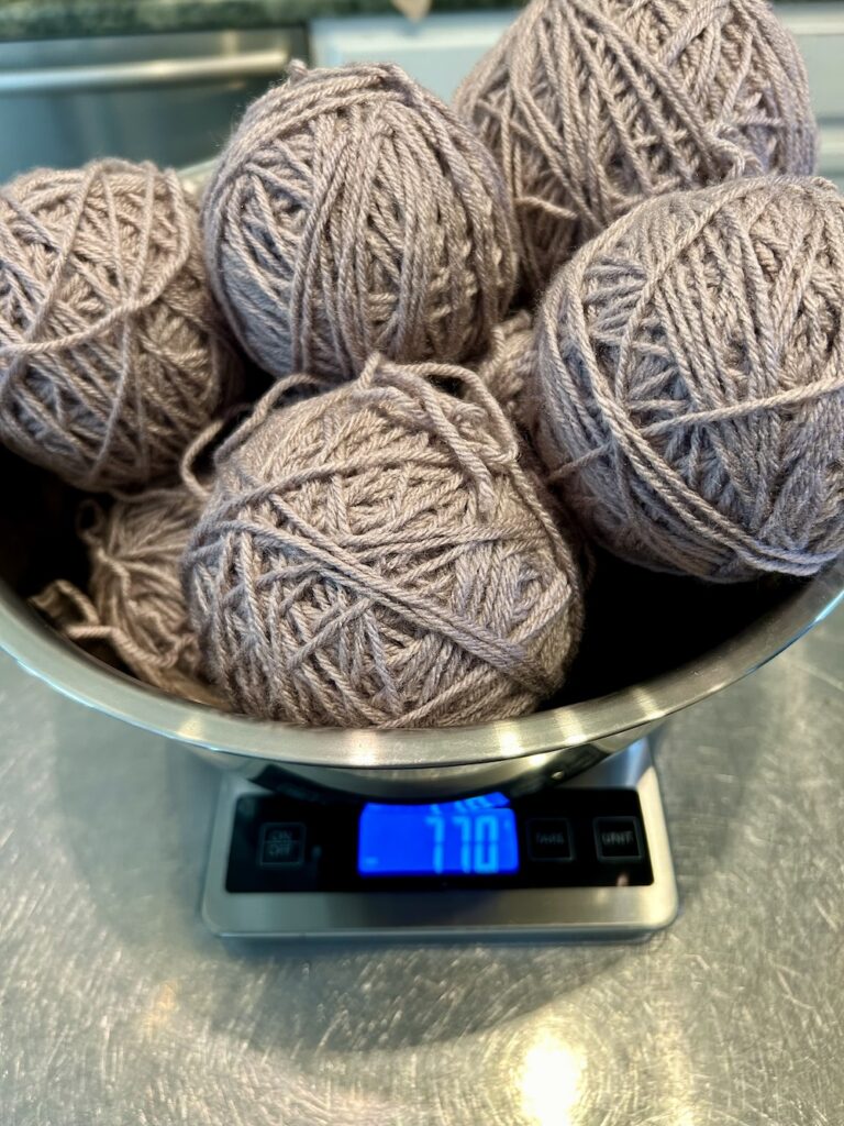 lavender gray yarn balls in a stainless steel bowl sitting on a kitchen scale.