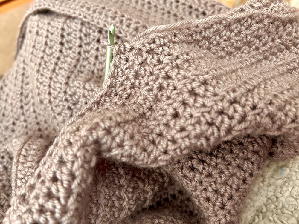 lavender gray yarn being crocheted into a cardigan with a crochet hook sticking out.