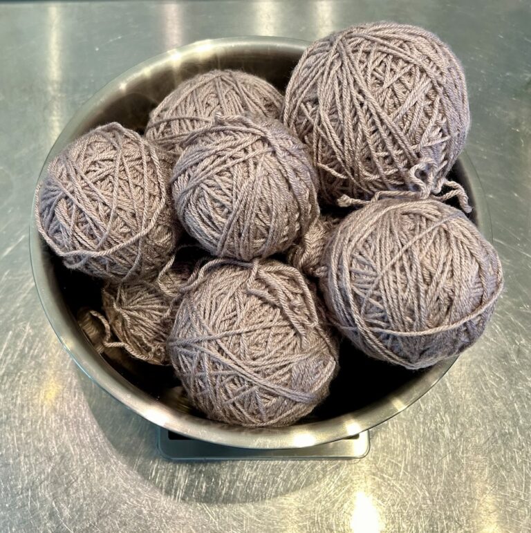 lavender gray yarn balls in a stainless steel bowl sitting on a kitchen scale.