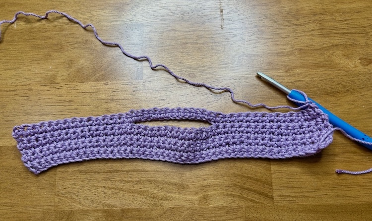 purple crochet strip with open loop section for hanging on a wooden background.