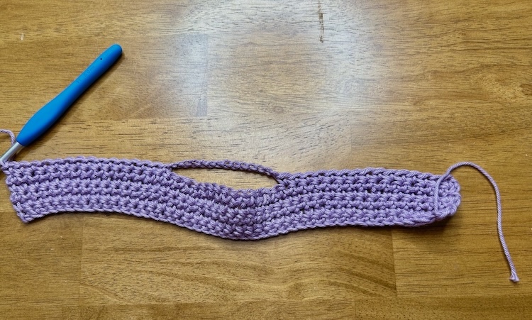 purple crochet strip with open loop section for hanging on a wooden background.