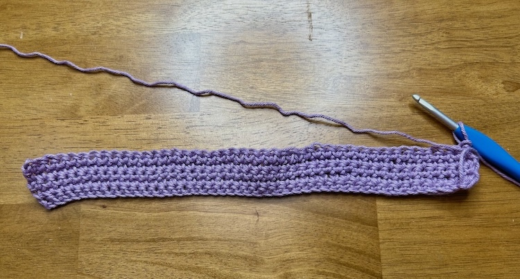 crocheted strip with purple yarn on a wooden background.