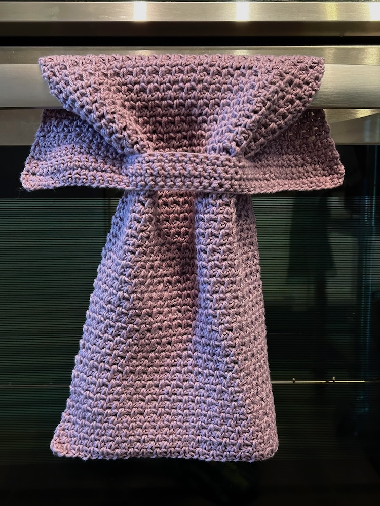 Purple crochet hand towel that stays put wrapped around a stainless steel oven handle.