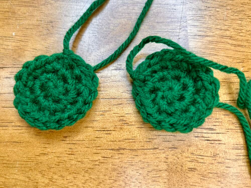 two dark green crocheted circles with 3 rounds of stitches.